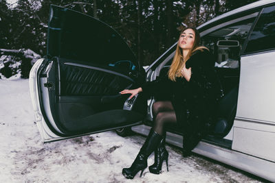 Full length portrait of young woman sitting in car during winter