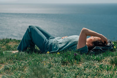 An adult woman, a pensioner, lies on the grass barefoot with a smile on her face on a sunny day