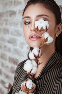 Close-up portrait of young woman with cotton plant against wall