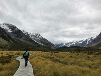 Rear view of man walking on footpath against sky