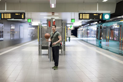Portrait of young man with basketball walking at railroad station platform