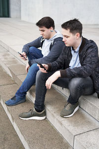 Full length of young man looking away while sitting on mobile phone