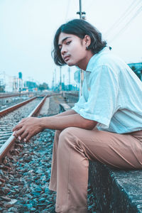 Side view of young woman sitting on railroad track