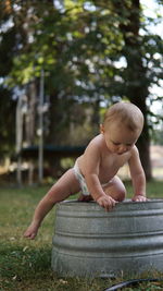 Toddler boy looking down and climbing off old galvanized bucket.