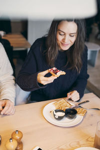High angle view of woman having waffle while sitting with friend at table in log cabin