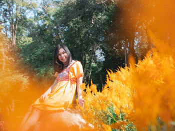 Portrait of young woman sitting against trees in forest