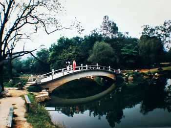 People on footbridge over river against sky