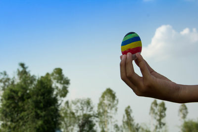 Low angle view of person hand holding multi colored egg against sky