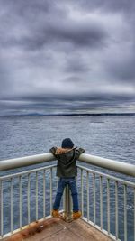 Rear view of man standing by railing against sea