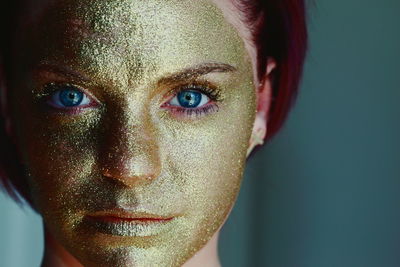 Close-up portrait of woman face with golden paint against green background