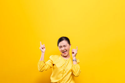 Young woman enjoying music against yellow background