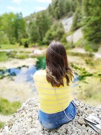 Rear view of woman sitting on cliff