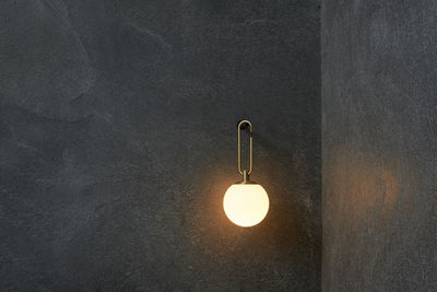 Low angle view of illuminated light bulb hanging on wall