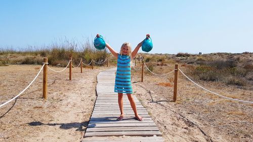 Girl holding baskets while standing on boardwalk at beach