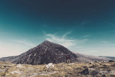 Rear view of male hiker standing on mountain against blue sky