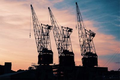 Low angle view of silhouette cranes against sky at sunset