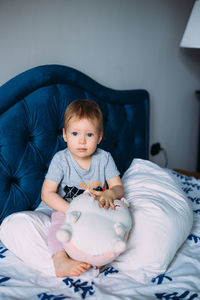 Little child is having fun, playing with soft toys on the couch at home.