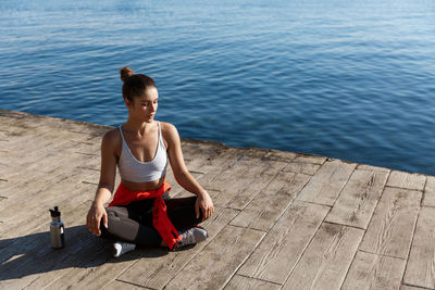 Full length of woman exercising while sitting against sea