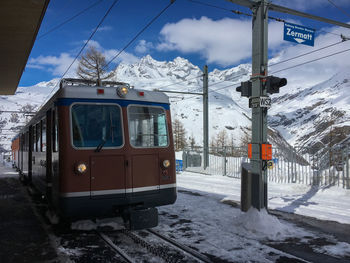Railroad tracks by snow covered mountain against sky