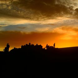 Silhouette people on landscape against orange sky