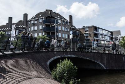 People on footbridge against sky in city