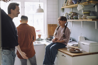 Father playing with daughter holding bread while sitting on kitchen counter at home