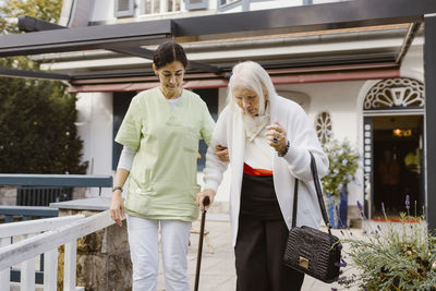 Mature woman supporting elderly woman walking with help of cane