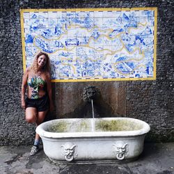 Portrait of smiling woman standing by old bathtub against wall