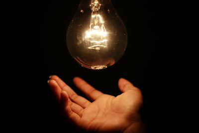 Close-up of hand holding light bulb against black background