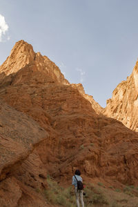 Rear view of hiker standing by rocky mountains against clear sky