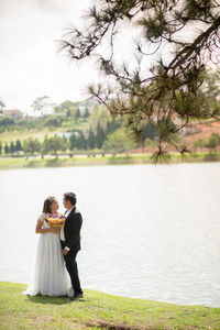 Newlywed couple standing against lake
