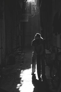 Rear view of woman walking on street amidst buildings at night