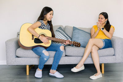 Full length of sisters playing guitar at home