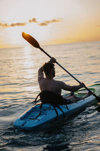 Man kayaking on sea against sky during sunset