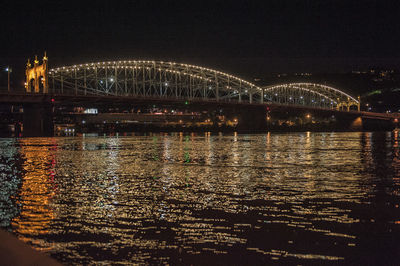 Illuminated bridge over river against sky at night