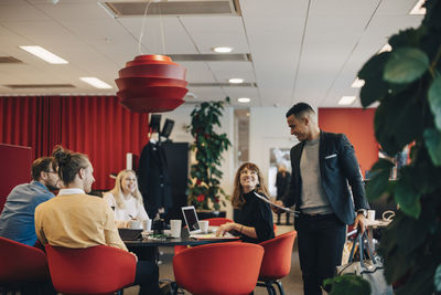 Smiling colleagues looking at businessman standing with bag and documents at office