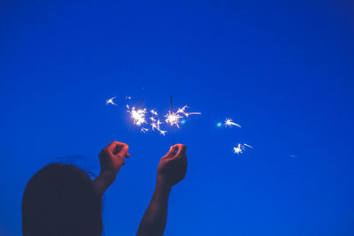 Rear view of woman holding sparklers against clear sky at night