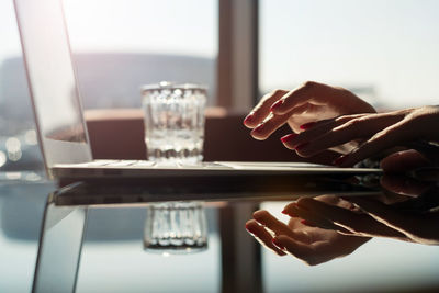 Close-up of woman using laptop at glass table