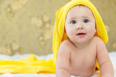 Curious baby girl lying with towel on head at home