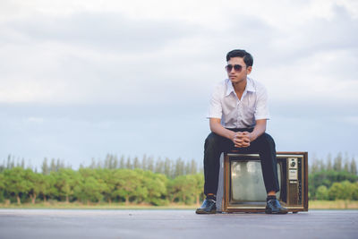 Side view of smiling teenage boy sitting on television set against sky