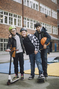 Boy holding push scooter with friends standing on skateboard in front of school building