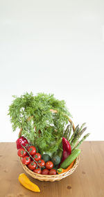 Fresh assorted vegetables in a basket on a wooden table, consumer vegetarian basket, tomatoes