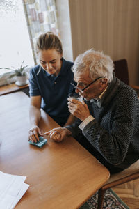 High angle view of senior man taking medicines while sitting with female caregiver at home