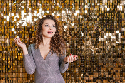 Festive mood in beautiful young woman on background shiny golden wall, smiles