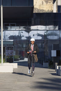 Latin businessman riding electric scooter between office buildings person