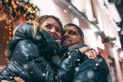 Couple romancing while standing against buildings at night during winter in city