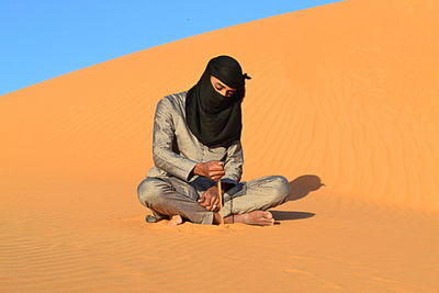 Young man sitting on sand against orange wall