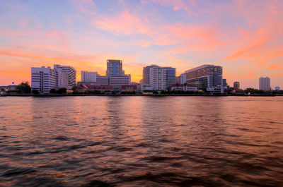 Scenic view of river by buildings against sky during sunset