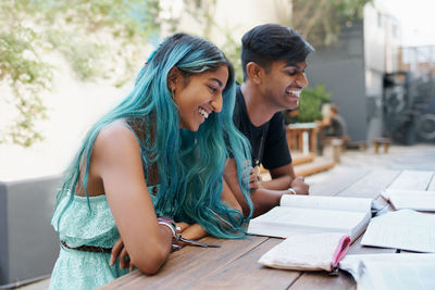 Smiling friends reading book at college