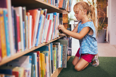 Schoolgirl looking for book for reading in school library. student selecting literature for reading